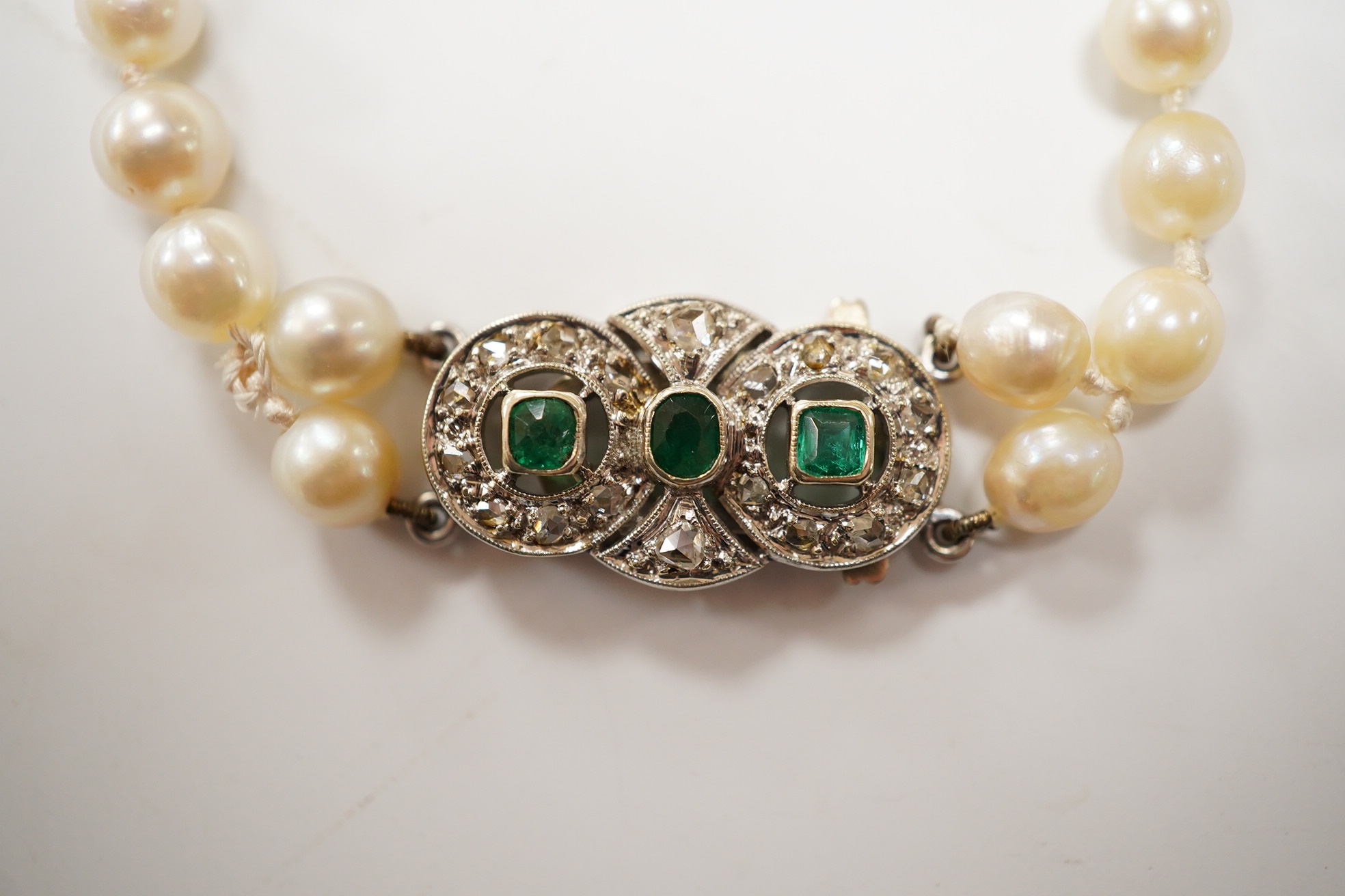 A single strand cultured pearl necklace, with and emerald and diamond cluster set white metal clasp, 76cm. Condition - fair.